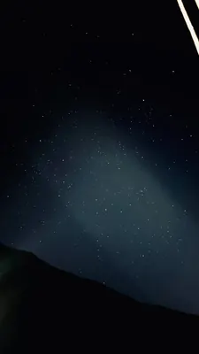 A star-filled night sky glows faintly above the black silhouette of a mountain ridge.
