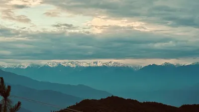 Dark blue mountain ridges overlap beneath a distant snowy range and textured clouds.