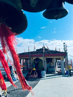 Temple bells and red devotional ribbons frame a sunlit shrine against a blue sky.
