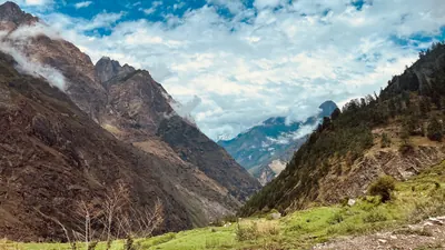 Steep rocky mountains frame a green valley that narrows into blue distance beneath bright clouds.