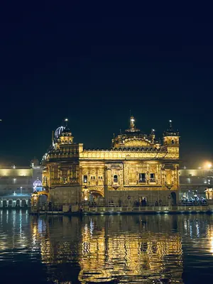 The illuminated Golden Temple at night reflected in still water beneath a deep blue sky.