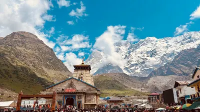 A stone temple and gathered visitors sit beneath a towering snowy mountain and bright clouds.